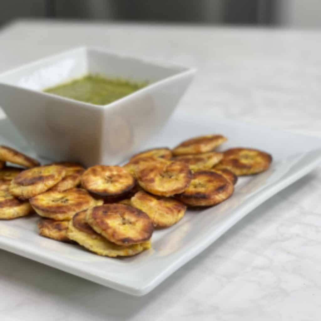 Baked plantains with mojo verde sauce on a white plate.